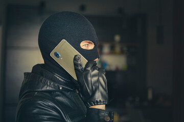 Young adult in black clothes with hidden face. Ill-intended fraudster uses mobile. Fraudster calls....