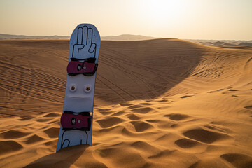 Desert safari tour in UAE. Snowboard used for sand boarding standing inserted in sand dune - 427380540