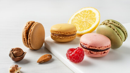 Variety of french macaroons with raspberry, nuts and lemon on white wooden table.