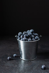 Fresh ripe blueberry in a metal small bucket on black background.