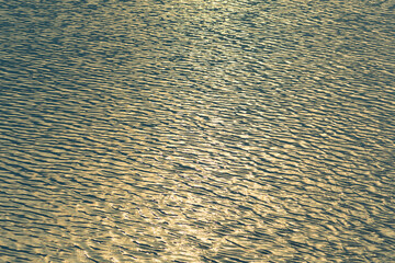 Small waves abstract or rippled water texture background, lake, sea or river with sunset or sunrise reflection 