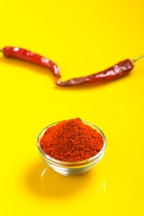 Dry Red chilli with chilli powder in glass bowl on yellow background.