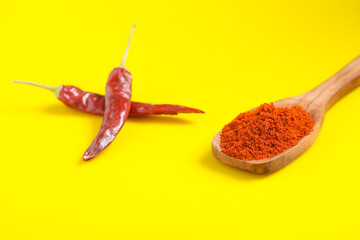Chilli powder in wooden spoon with dry red chilly on yellow background.