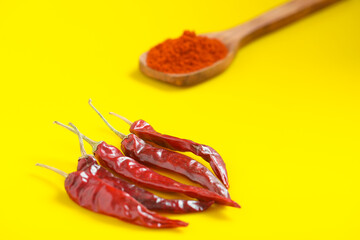 Chilli powder in wooden spoon with dry red chilly on yellow background.