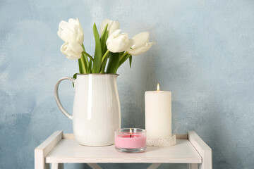 Beautiful white tulips and burning candles on wooden table against light blue background