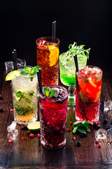 Selection of gin tonic with blackberries, with orange, with lime and mint leaves. In glasses on a rustic wooden background