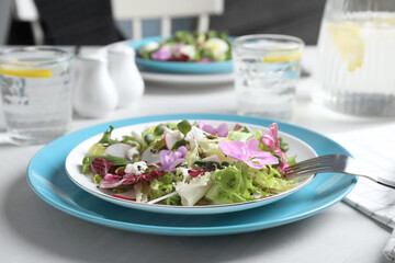 Fresh spring salad with flowers served on white table, closeup