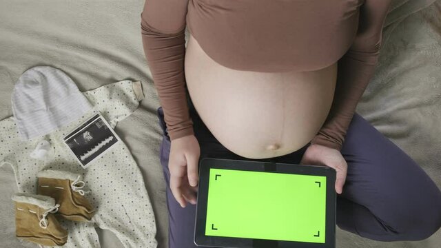 expecting pregnant woman with large belly using tablet with chromakey on bed