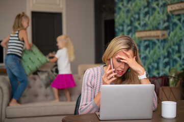 Exhausted woman trying to work at home while kids are playing in background