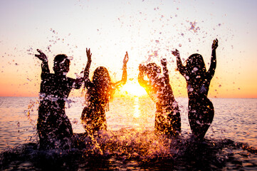 Happy friends splashing inside water on tropical beach at sunset  - Group of young people having...