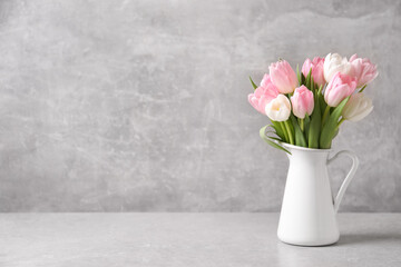 Beautiful bouquet of tulips in jug on light table. Space for text