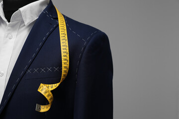 Semi-ready jacket with tailor's measuring tape on mannequin against grey background, closeup. Space...