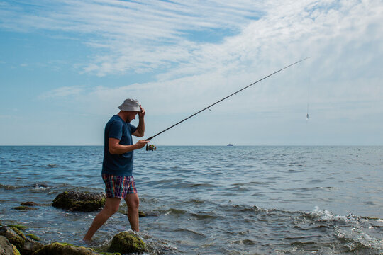 man with fishing rod. stands on the ankle in sea water on the stones