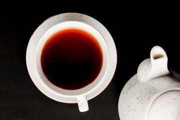 White tea cup with tea pot over black background.