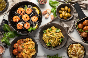 Assortment of Italian pasta with traditional snacks and sauces for dinner on white wooden background.