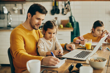 Working father taking notes while his small daughter is siting on his lap at home.