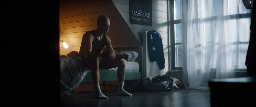 WIDE bored Caucasian kid teenager boy playing with football ball in his attic bedroom at home. Shot with 2x anamorphic lens