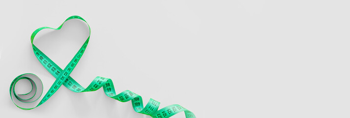 Green plastic measure tape with metric scale in the shape of a heart over on grey background. Top...