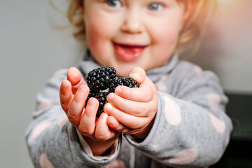 A little girl holds fresh blackberries in her hands with a smile on her face.