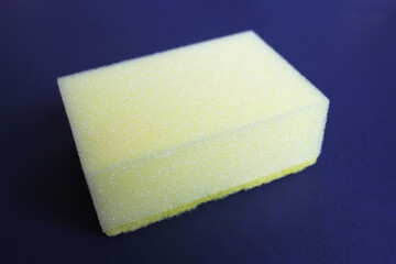 Yellow sponge for washing dishes on a dark blue background, close-up, side view. New, clean, dry rectangular sponge. Kitchen utensil.