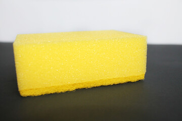 Yellow sponge for washing dishes on a black surface on a white background, close-up, side view. New, clean, dry rectangular sponge. Kitchen utensil.