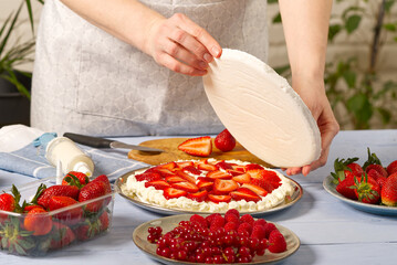 woman baker add a new layer of meringue base in strawberry cake. Homemade strawberries cake made from meringue cake and cream with strawberries. home cooking concept