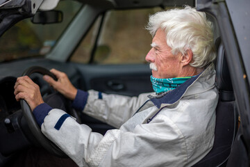 A mature man driving an SUV car, keeping his hands on the steering wheel.