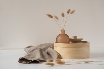 Rabbit tail grass in beautiful tan vase, wooden storage box, neutral beige blanket against white...