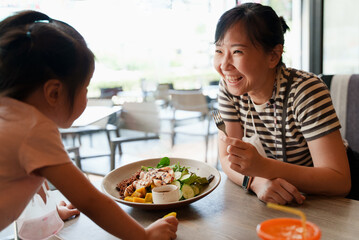 Happy loving Asian family. Mother and her daughter child girl are eating salad at the restaurant.