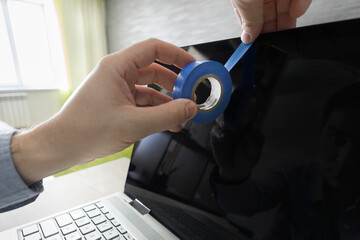 Spying on privacy via webcam. Human hand blocks a webcam of laptop by an adhesive tape. persecution...