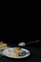 Pilaf on a black background. A spoonful of pilaf over a plate. Creative food photography on dark background