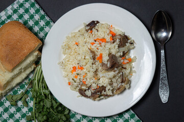 Pilaf on a black background. Pilaf with meat on a white plate. Food on a dark background