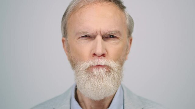 Serious man squinting eyes in studio. Senior gentleman looking camera indoors.