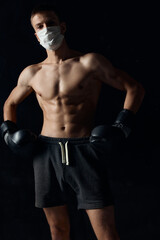 Fototapeta na wymiar sporty man in medical mask and in boxing gloves on black background shorts 