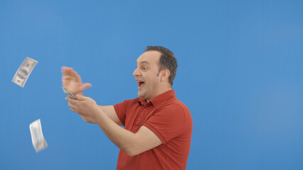 Young man with beard in front of a blue background who is cheerfully gesturing while handing out...