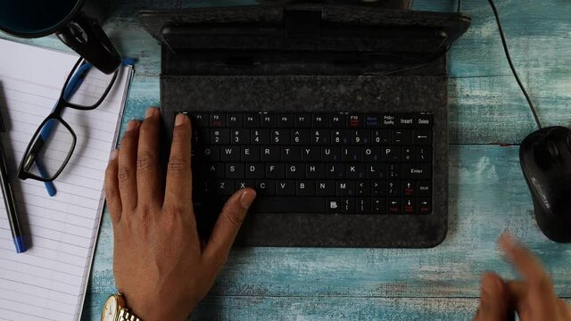 Top view of hands of an Indian man typing in keyboard of mini computer on wooden table