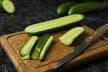 Board with ripe cucumber and knife on black smokey table