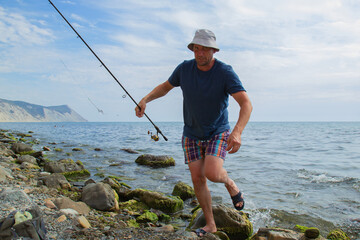 a man with a fishing rod comes out of the water on a rocky shore