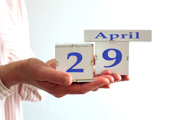 Calendar for April 29 : women's hands hold cubes with the number 29, the name of the month of April in English, side view