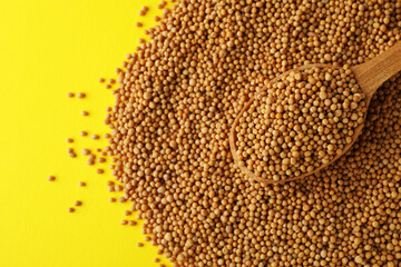 Wooden spoon with mustard seeds on yellow background