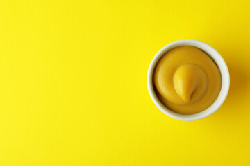 Bowl with mustard on yellow background, top view