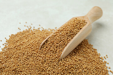 Wooden scoop with mustard seeds on white textured background