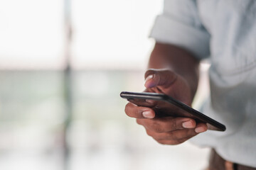 A businessman standing at the window playing a smartphone discussing a business investment project.
