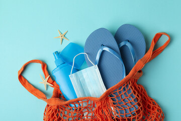 Bag with sea accessories, sunscreen and mask on blue background