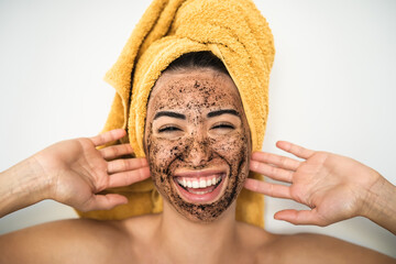 Young  woman applying coffee scrub mask on face - Happy girl having skin care spa day at home -...