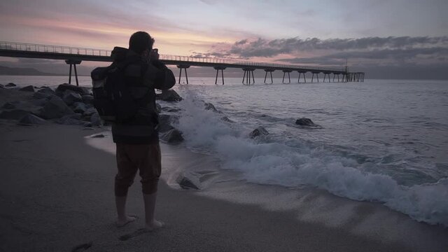 Landscape photographer wearing a backpack taking photos of the sunrise at the beach