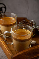 Iced Dalgona coffee drink on wooden tray background. Instant coffee or espresso powder whipped with sugar and hot water. Coffee with milk latte, cappuccino. Two glass cups with double walls. Breakfast