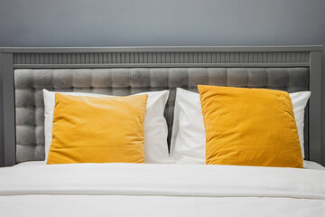 Bed with gray color velvet headboard and bright yellow pillows.