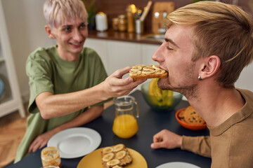 Happy homosexual partner feeding caucasian young man