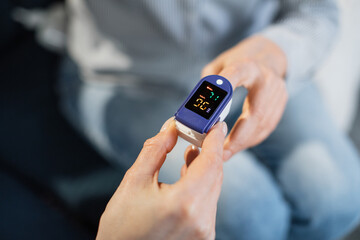 Pulse oximeter, finger digital device to measure oxygen saturation in blood. Close up view of doctor hand measuring oxygenation level of female unrecognizable patient for exclusion of pneumonia.